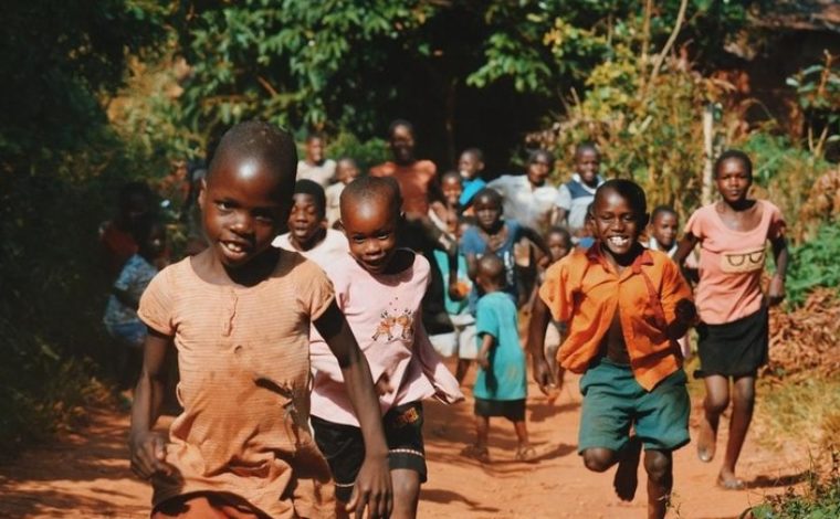 Children running and walking on brown sand surrounded with trees during daytime